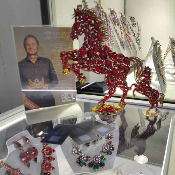 A close-up of a red rhinestone horse centerpiece featured alongside exquisite jewelry and a portrait of designer Roman Matouš