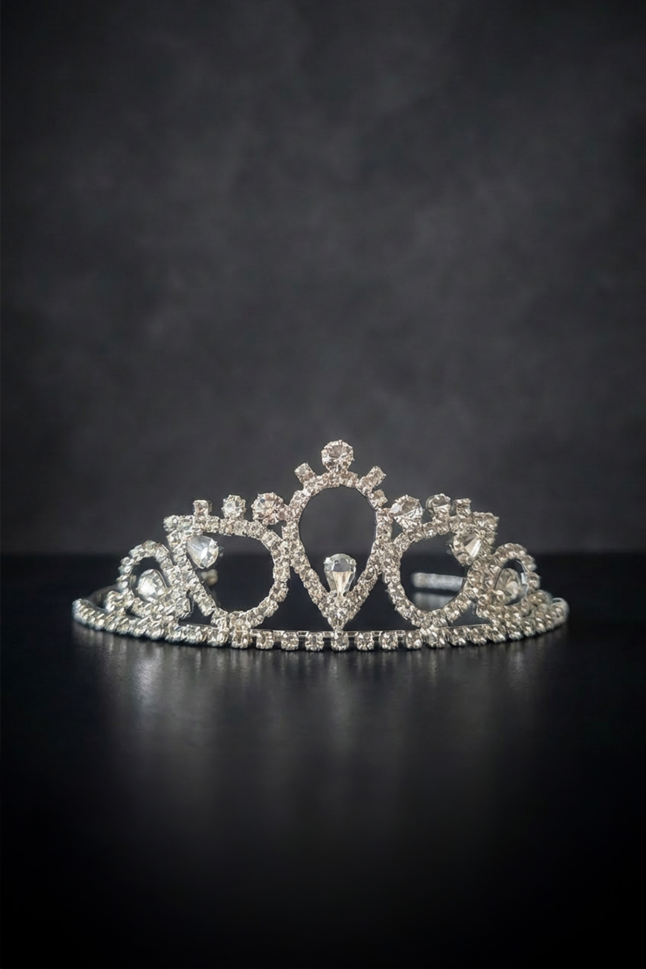 Silver tiara with a clear crystals and a prominent central stone set in a polished metal frame.